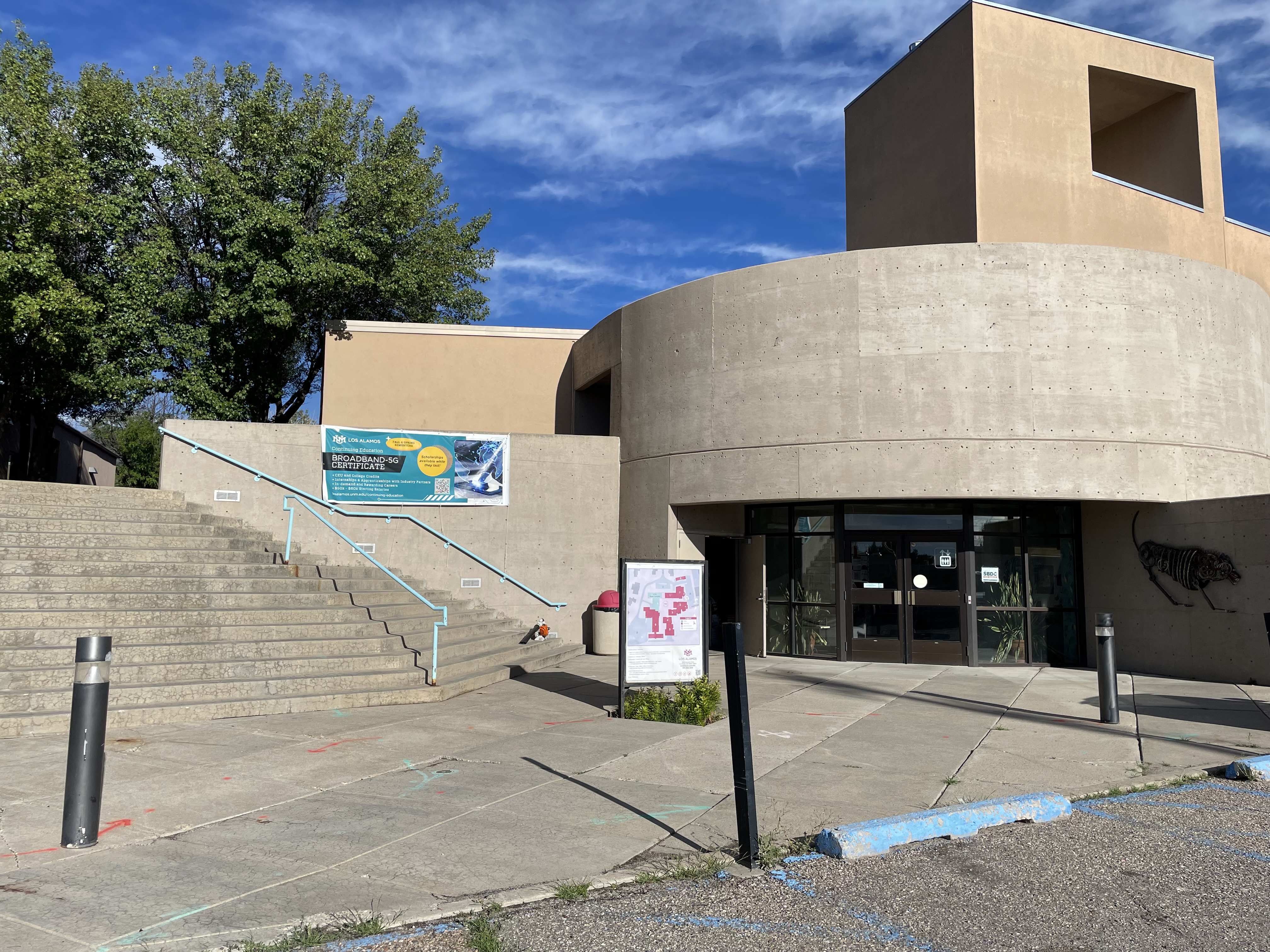 A banner announcing the Broadband-5G Certificate program is displayed on the front wall of UNM-LA campus.